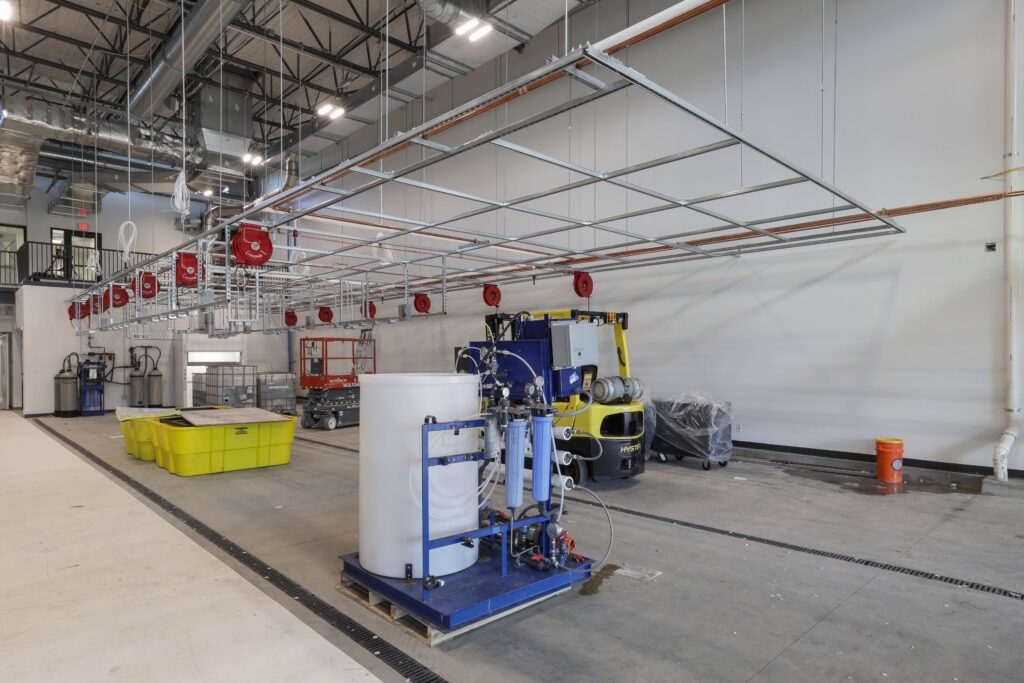 An industrial facility interior with overhead reel systems, a yellow forklift, and a mobile water filtration unit on a blue skid.