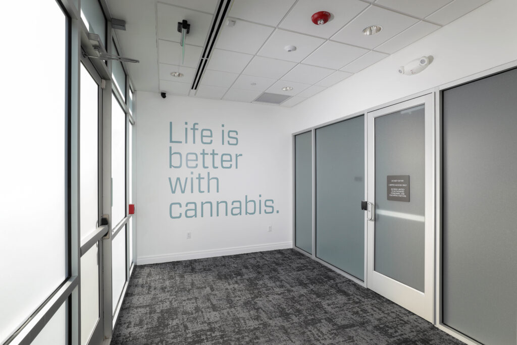 Office hallway featuring a wall decal that reads, “Life is better with cannabis,” next to a glass door with a “Do Not Enter” sign.