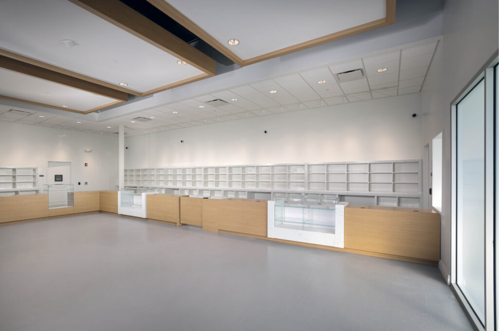 An empty retail space with long wooden counters, glass display cases, and white shelving along the back wall.