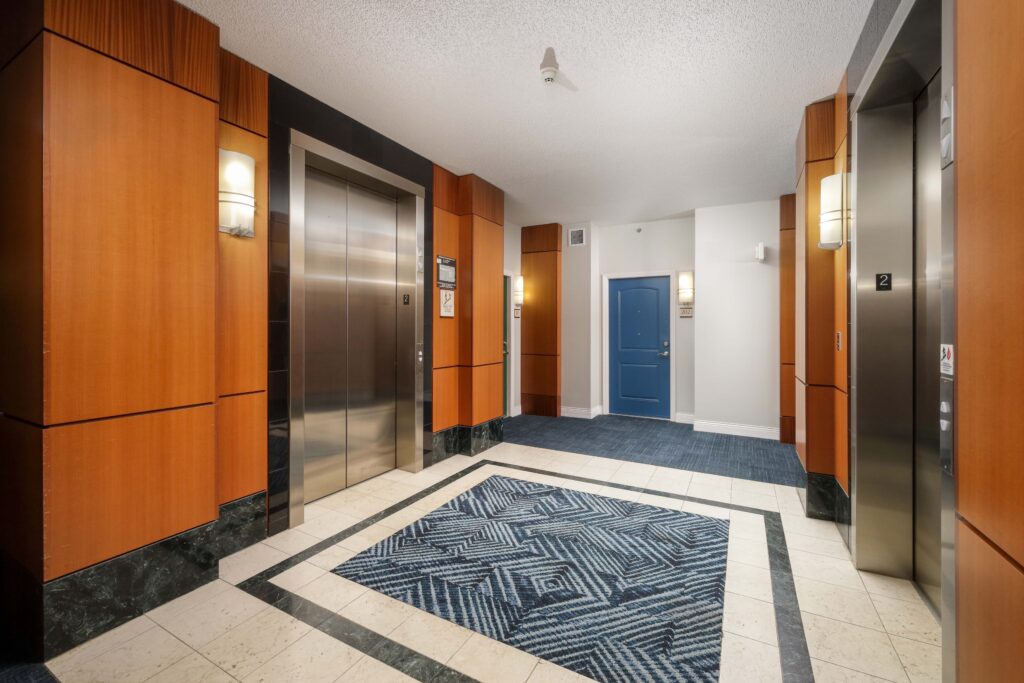 Elevator lobby with two stainless steel elevators, wood-paneled walls, and a blue door at the end of the hallway.