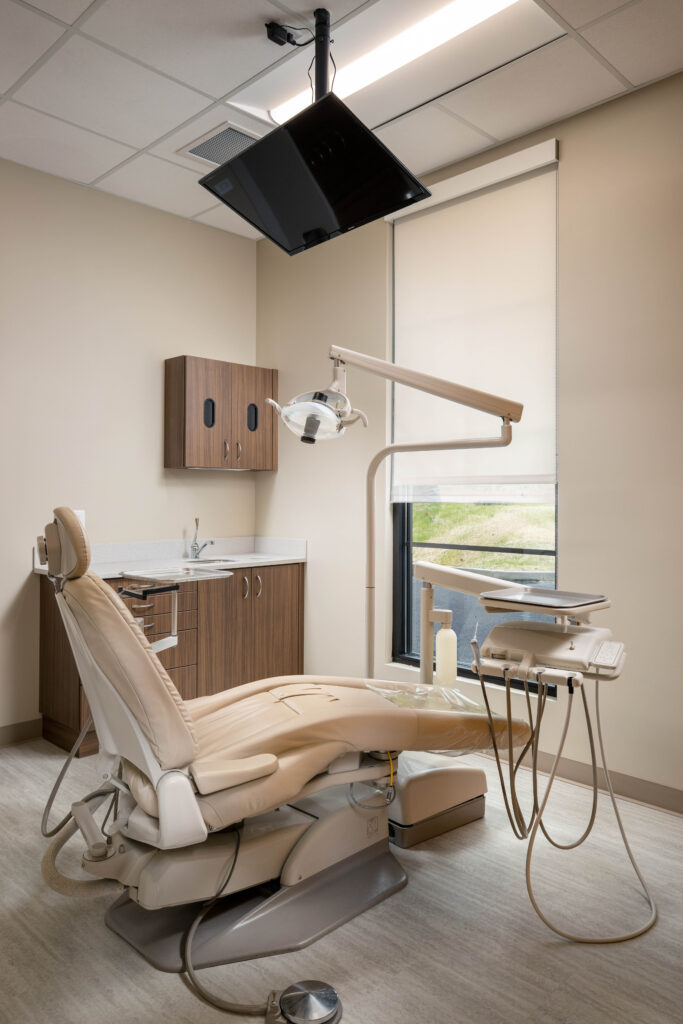 Dental examination room featuring a reclining chair, dental lamp, equipment tray, and sink counter.