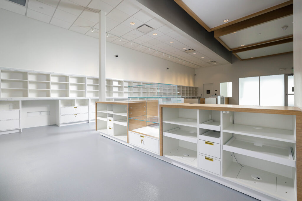 An empty retail space featuring white shelving units with light wood countertops and a central glass display case.