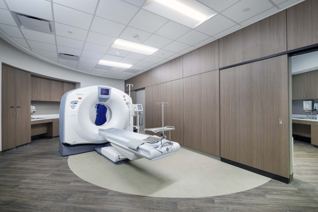 A CT scanner in a medical imaging room with a patient bed extended in front of the machine.