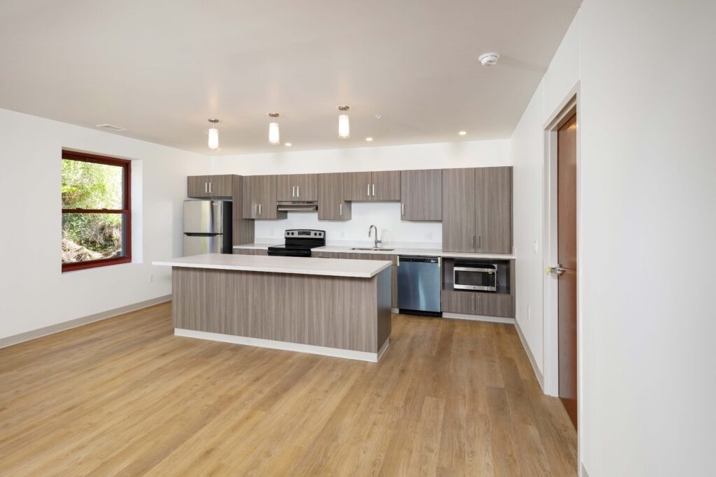 Modern kitchen with wood-finish cabinets, an island with a white countertop, and stainless steel appliances.