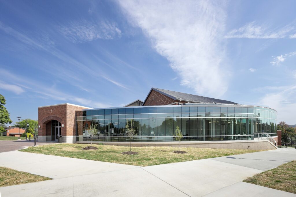 A modern building with a curved glass facade and a brick entrance section under a blue sky.