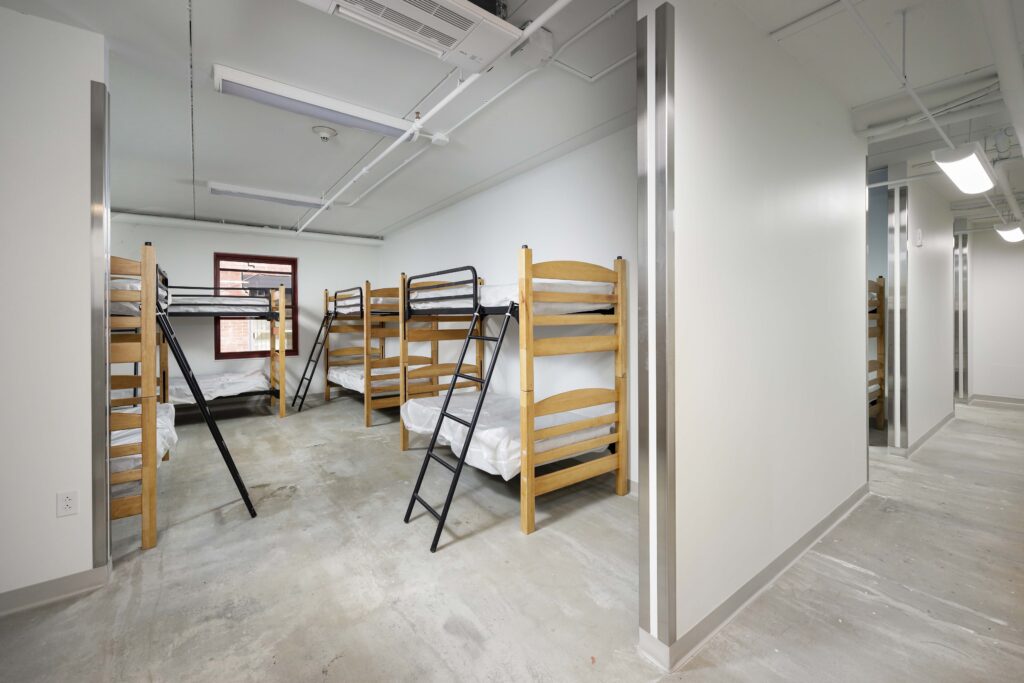 A dormitory room with several wooden bunk beds, each with a metal ladder and white bedding.