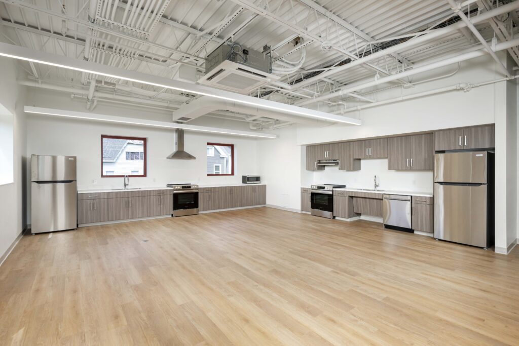 Large kitchen space with wood-toned cabinets, stainless steel appliances, and an exposed industrial ceiling.