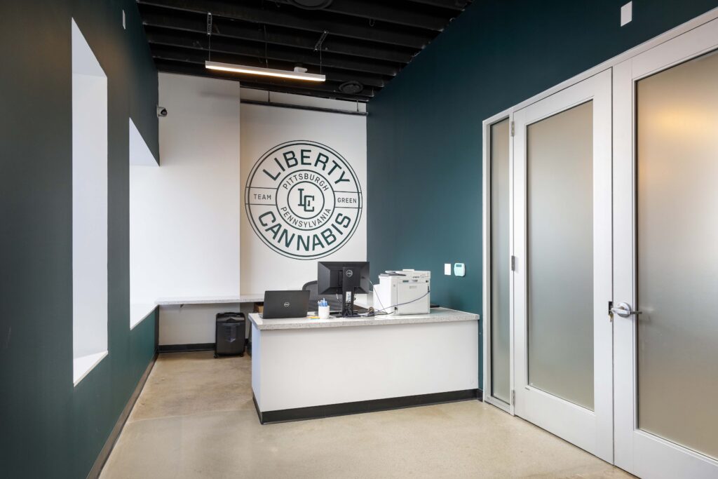 Reception desk at Liberty Cannabis Pittsburgh with a computer, printer, and company logo on the wall.
