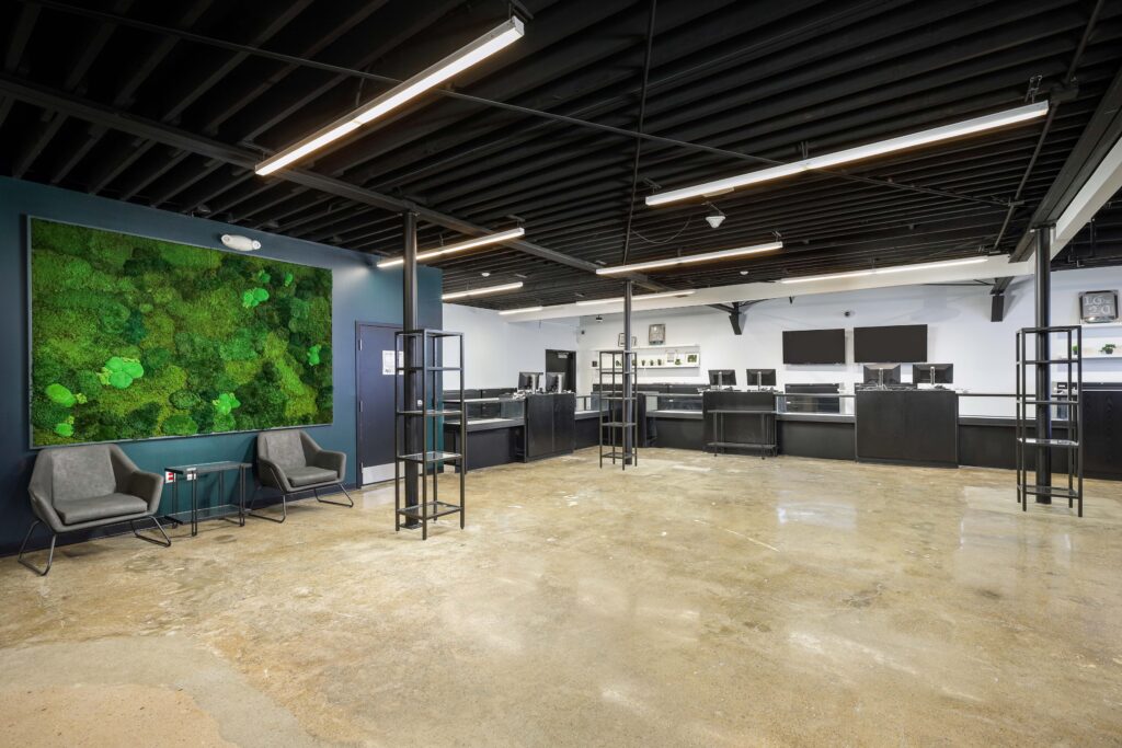 Open retail floor with a large living moss wall, two grey armchairs, and a row of service counters along the back wall under a black open-joist ceiling.