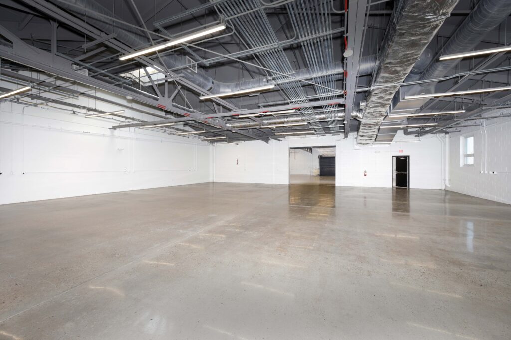 An empty industrial warehouse space with white walls, polished concrete floors, and exposed ceiling ductwork.