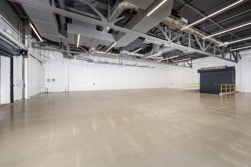 An empty industrial warehouse space with polished concrete floors, white walls, and exposed ductwork on the ceiling.