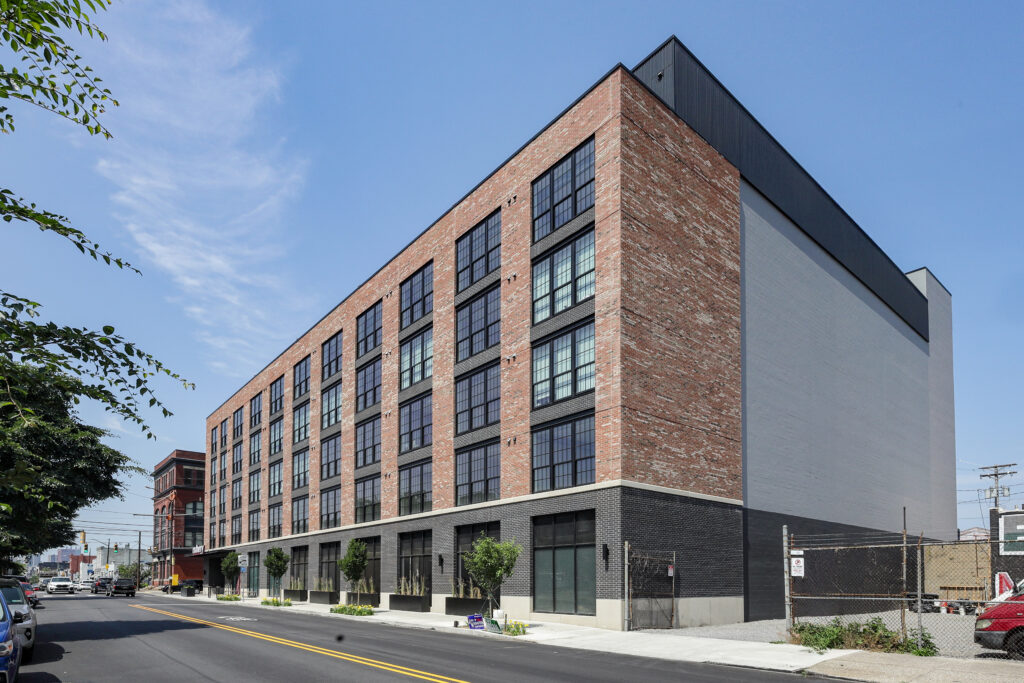 A multi-story building with a red brick facade, large windows, and a black ground floor, situated on a street corner.