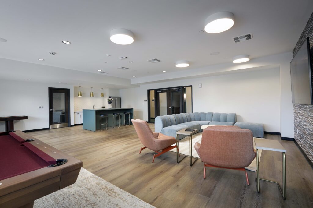A lounge area featuring a pool table, two armchairs, a curved sofa, and a kitchen island with bar stools.