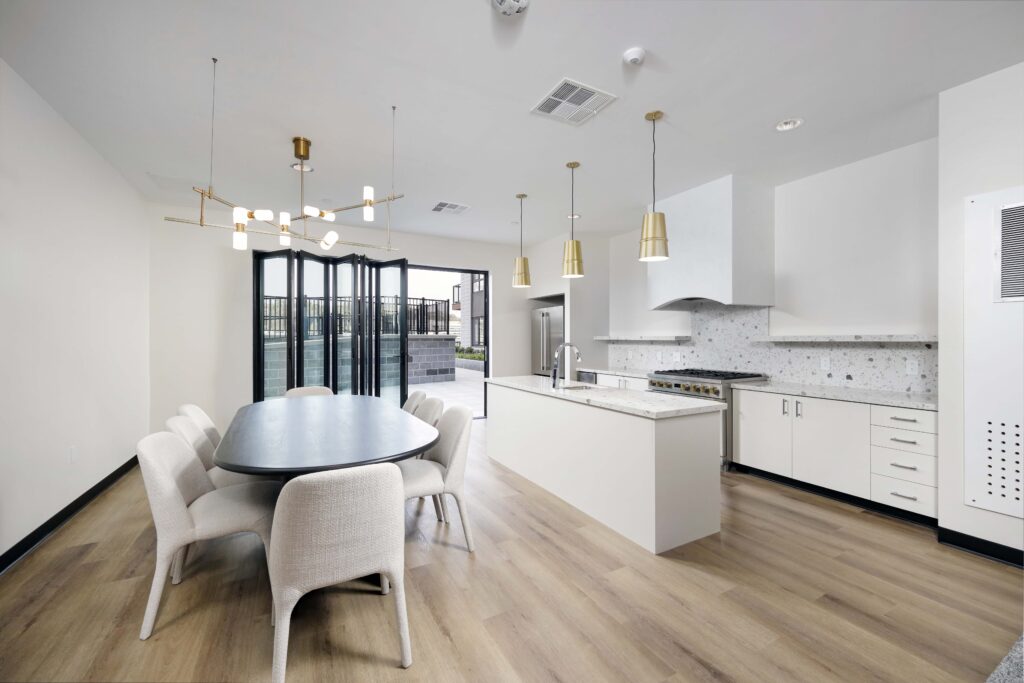 Open-concept kitchen and dining area featuring a black oval table with six chairs, a central island with a sink, and bi-fold glass doors opening to a patio.