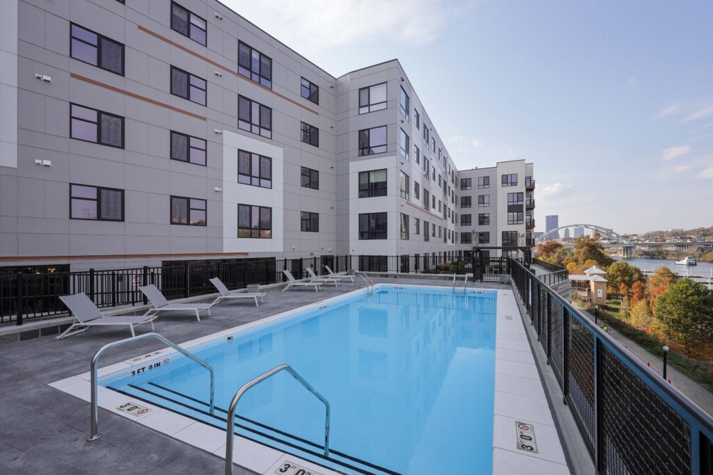 Outdoor swimming pool on an apartment building terrace overlooking a river and bridge.
