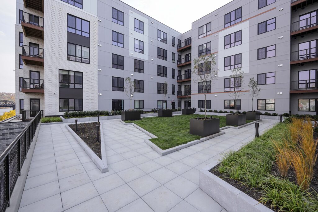 Courtyard of a multi-story apartment building with a paved patio, a small central lawn, and container plants.