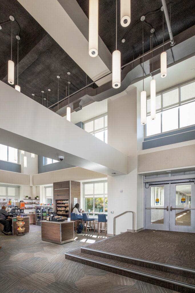 Modern cafe interior with a service counter, a patron seated at a window bar, and a set of double glass doors leading outside.
