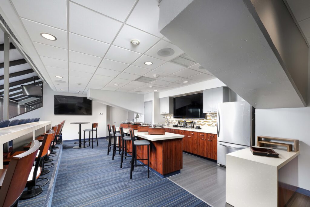 A kitchenette and lounge area with a counter, high stools, bar tables, and wall-mounted televisions.
