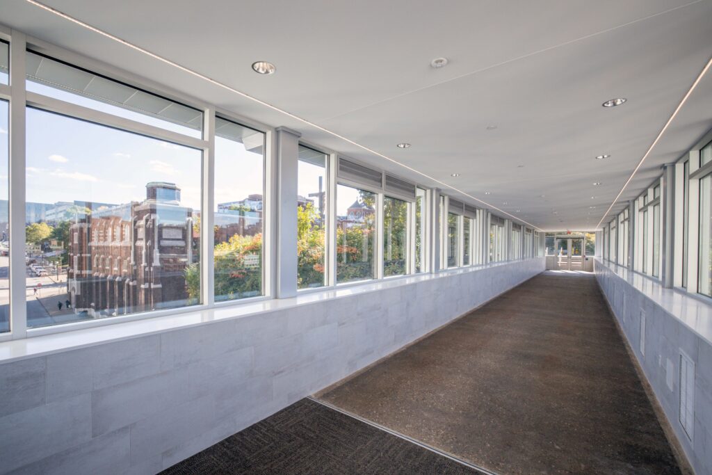 A long, empty indoor corridor with large windows looking out onto a city street and trees.