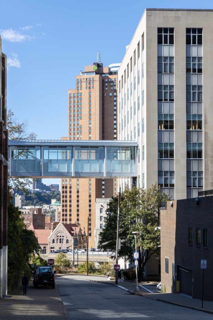 A glass-walled skywalk connects two tall buildings over a street in a city.