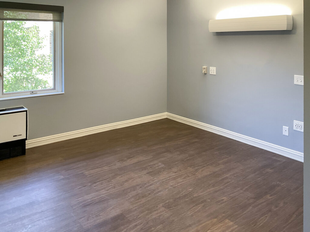 An empty room with light blue walls, wood-look flooring, a window, and a wall-mounted light fixture.