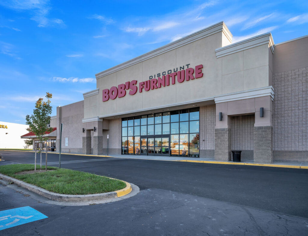 Exterior of a Bob’s Discount Furniture store with glass storefront windows and a paved parking lot.