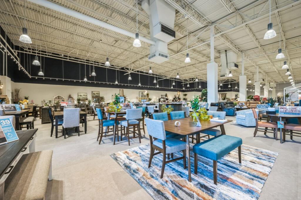 A furniture showroom floor displaying multiple dining sets and sofas arranged on area rugs.