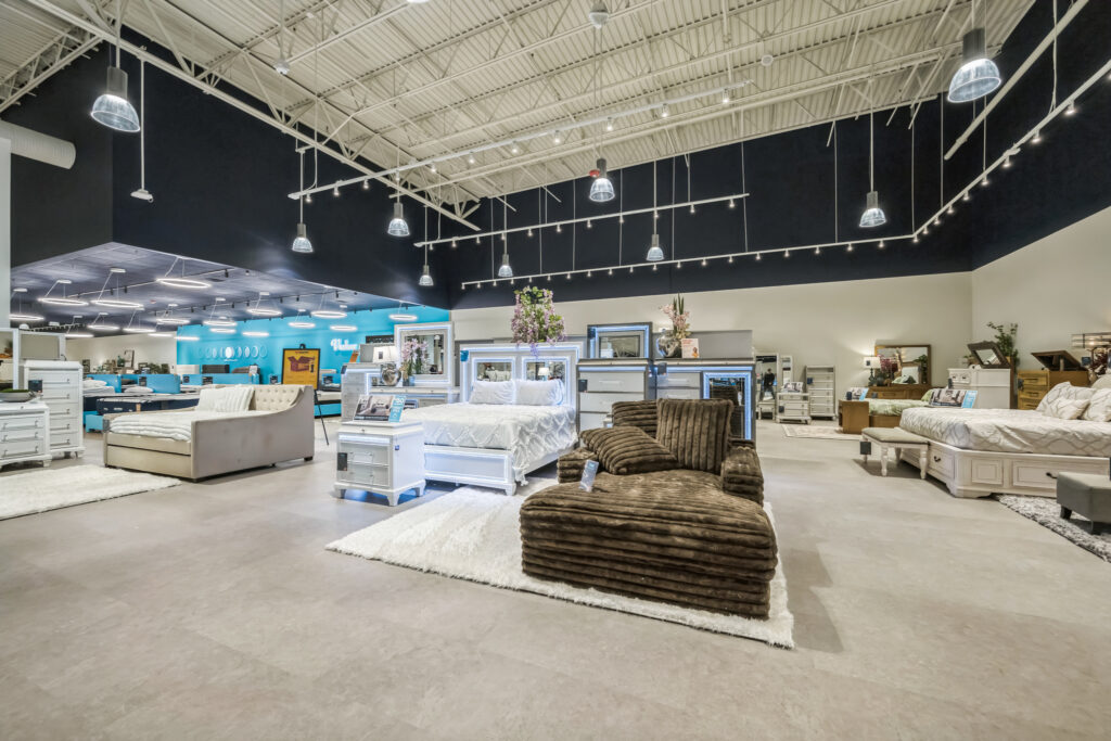 A showroom floor displaying various bedroom sets, including beds, dressers, and a brown corduroy chaise lounge.