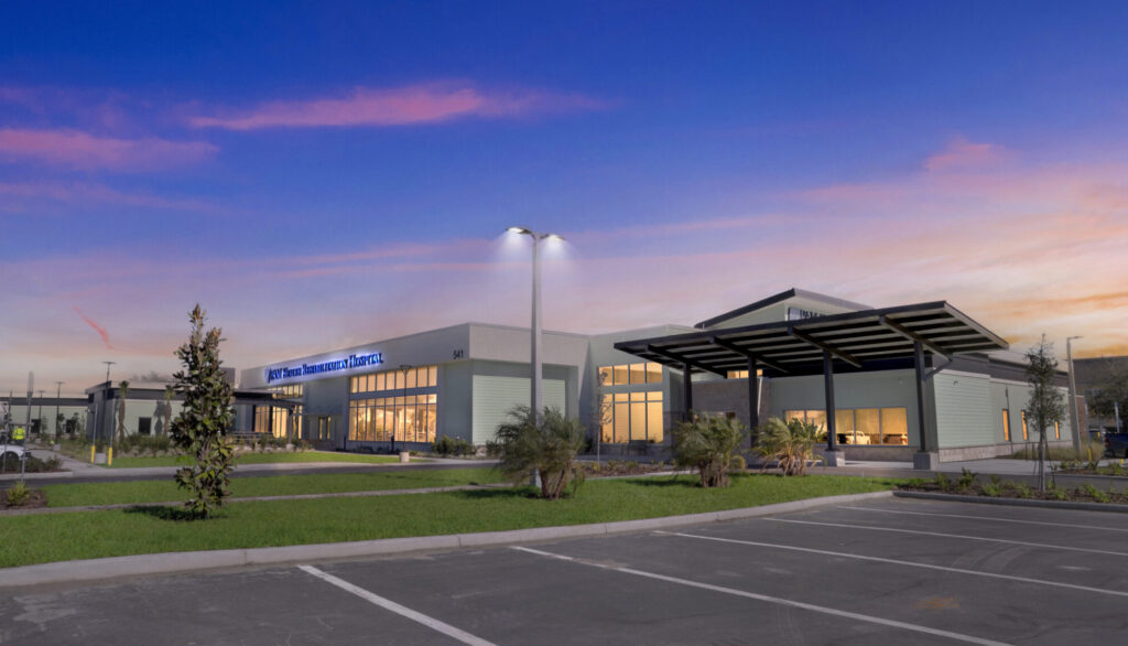 Exterior of Encompass Health Rehabilitation Hospital at dusk, featuring a modern building with a covered entrance and parking lot.
