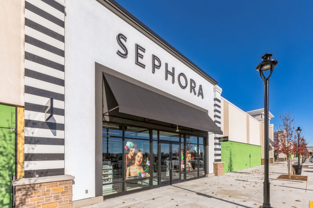 Exterior of a Sephora storefront with black and white striped accents, a black awning, and window displays under a clear blue sky.