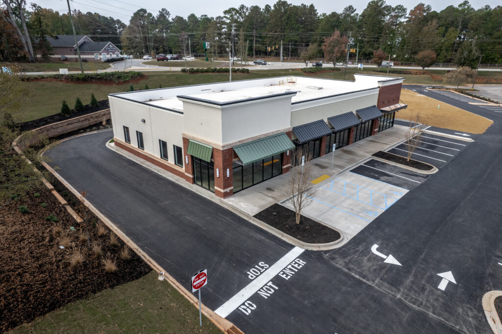An aerial view of a vacant single-story commercial strip mall with a surrounding parking lot.