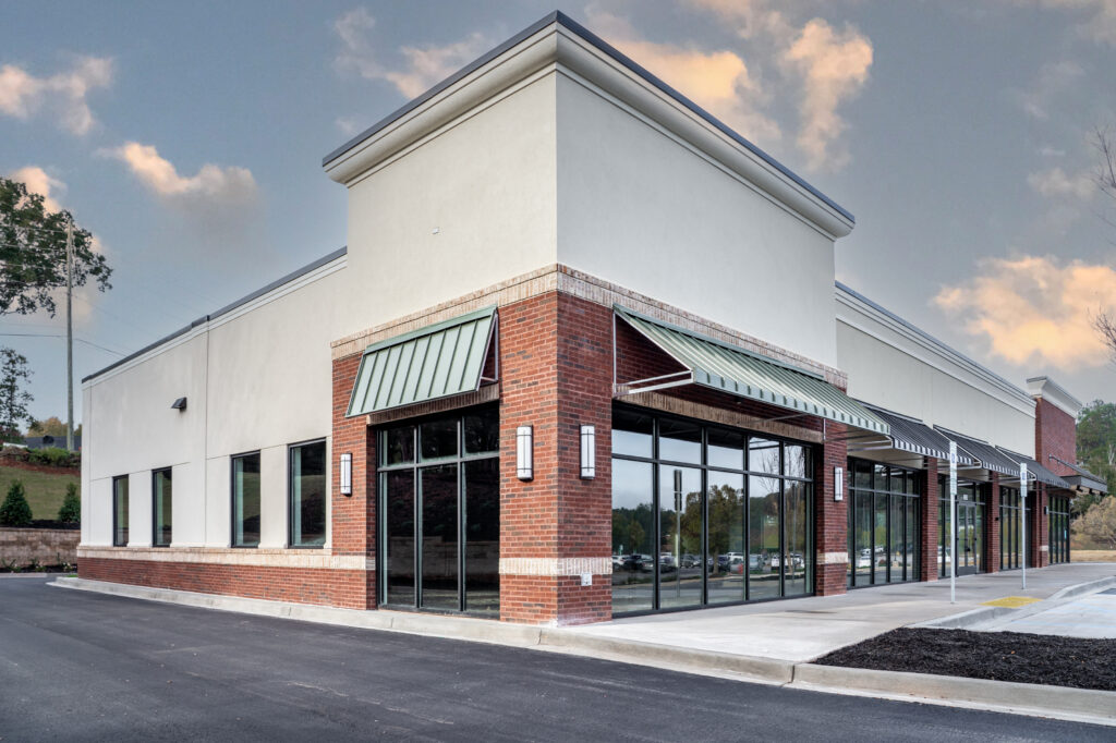 A vacant retail storefront with a brick and stucco exterior, metal awnings, and large glass windows.