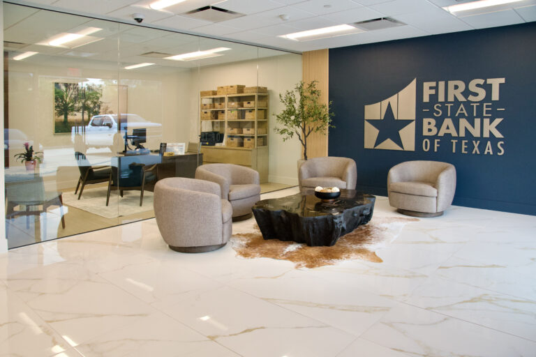 Lobby of First State Bank of Texas featuring a seating area with three chairs and a coffee table, and an enclosed office space visible behind a glass wall.