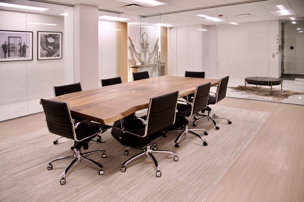 Modern conference room featuring a large wooden live-edge table surrounded by eight black office chairs on a light-colored rug.