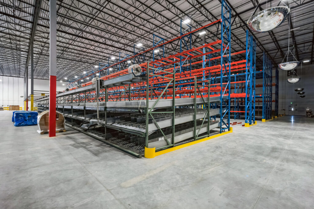 Large warehouse interior featuring rows of empty industrial pallet racking with blue frames and red horizontal beams.