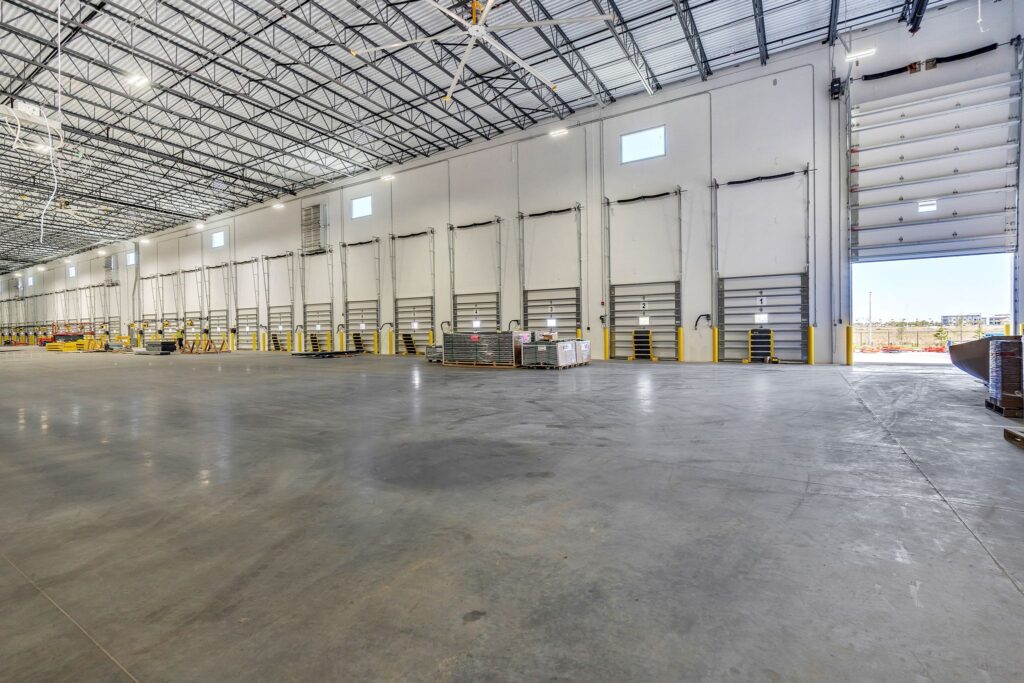 Empty warehouse interior with high ceilings, concrete floors, and a row of numbered loading dock doors.