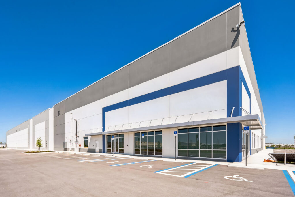 Modern industrial warehouse building with a gray and white facade, large windows, and marked accessible parking spaces in the foreground.