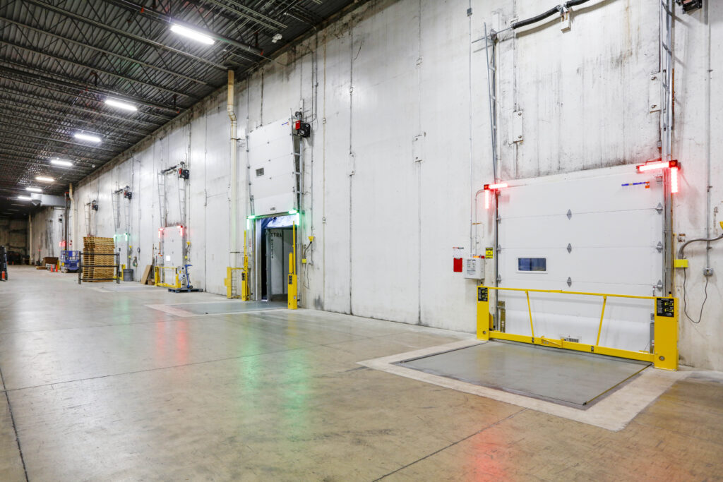 A row of loading dock doors with red and green indicator lights in a large industrial warehouse.