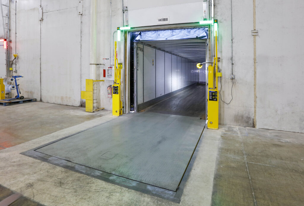 A loading dock with a metal dock leveler connected to the back of an empty semi-trailer.