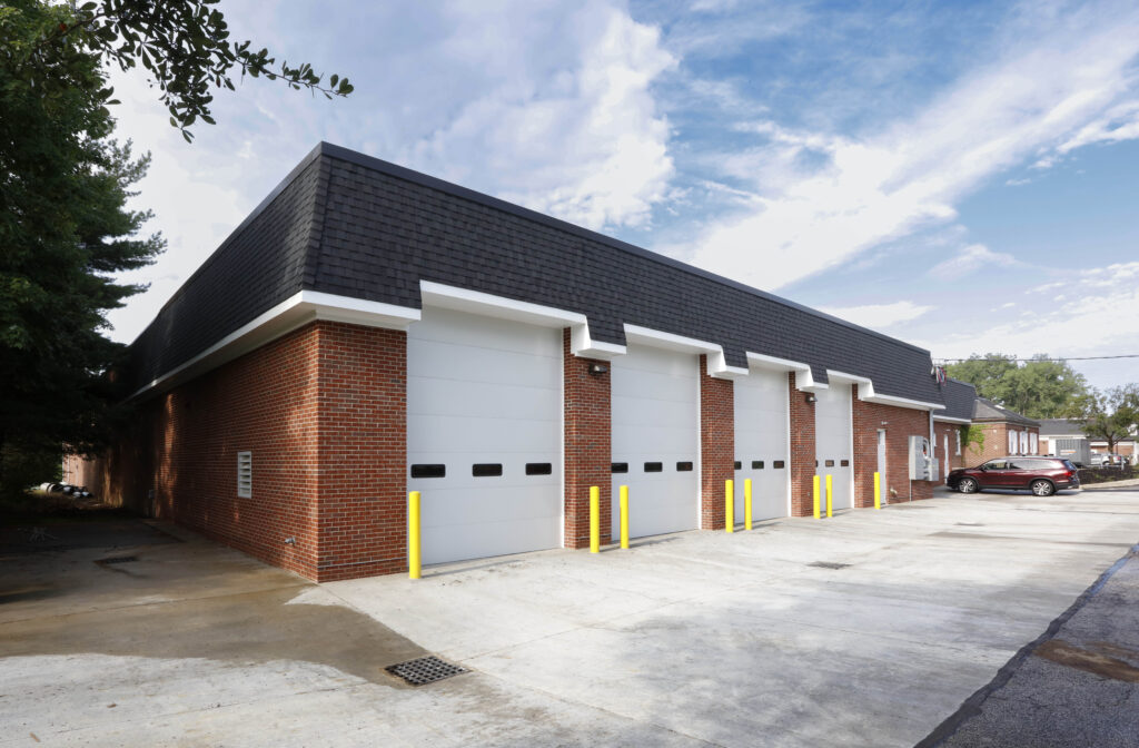 A red brick building with four white garage doors and a black mansard roof.