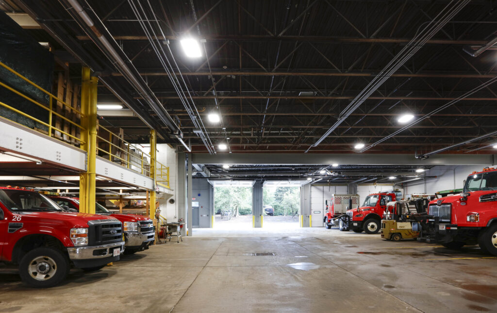 Inside a maintenance garage with red fire trucks and a forklift parked in bays.
