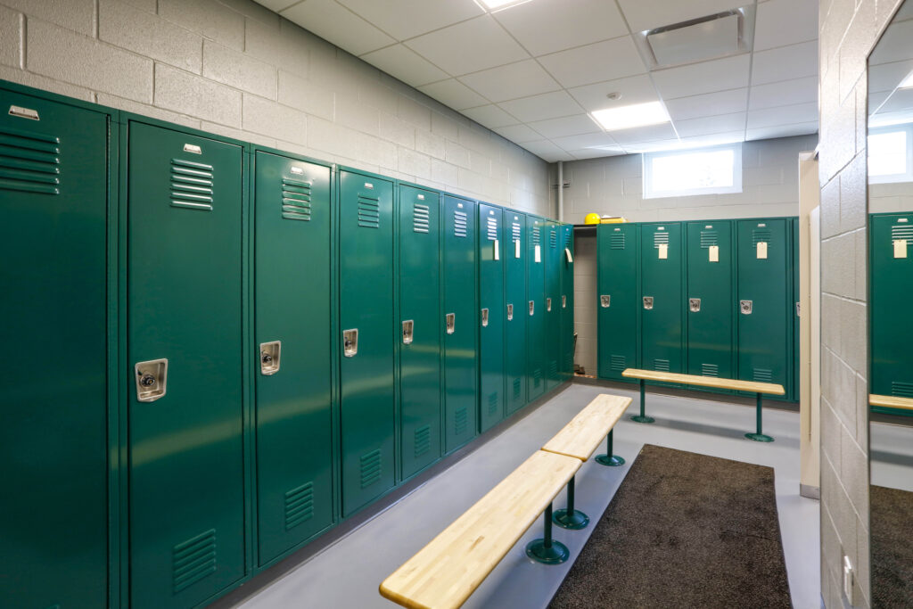 A row of green lockers in a changing room with wooden benches.