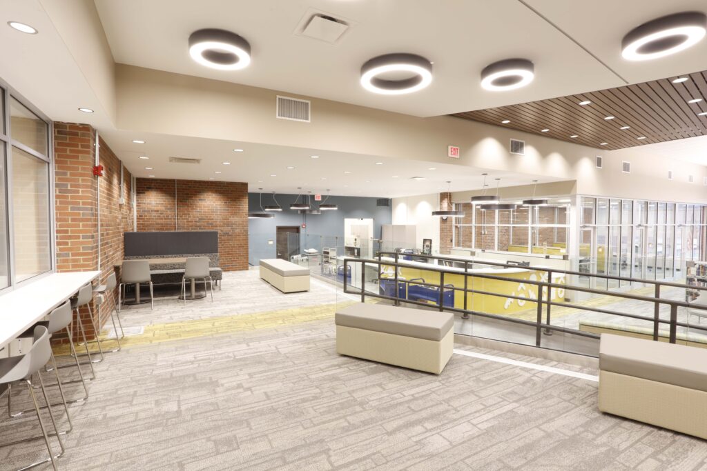 Modern library interior with study tables, bench seating, and a glass-enclosed service desk.