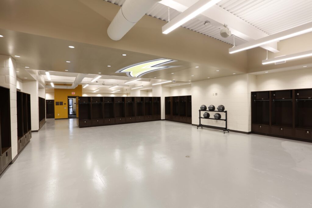 A spacious locker room with rows of dark wooden lockers, a polished grey floor, and a rack holding four medicine balls.