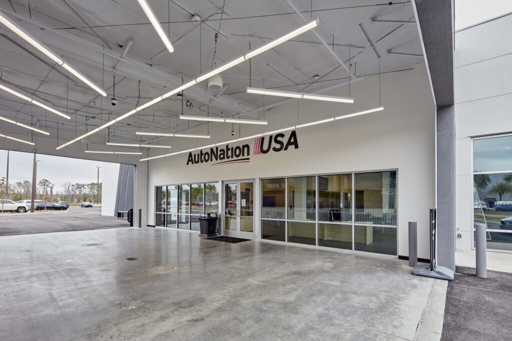 Exterior view of an AutoNation USA dealership entrance with a large covered concrete arrival area.