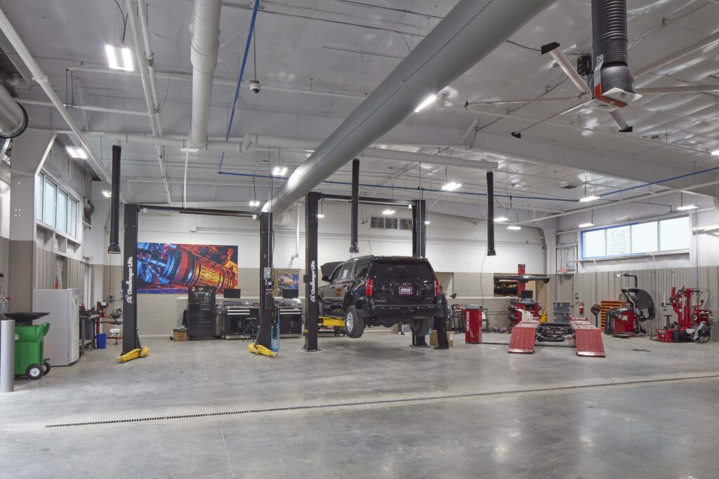 A black SUV elevated on a car lift in a spacious automotive service center.