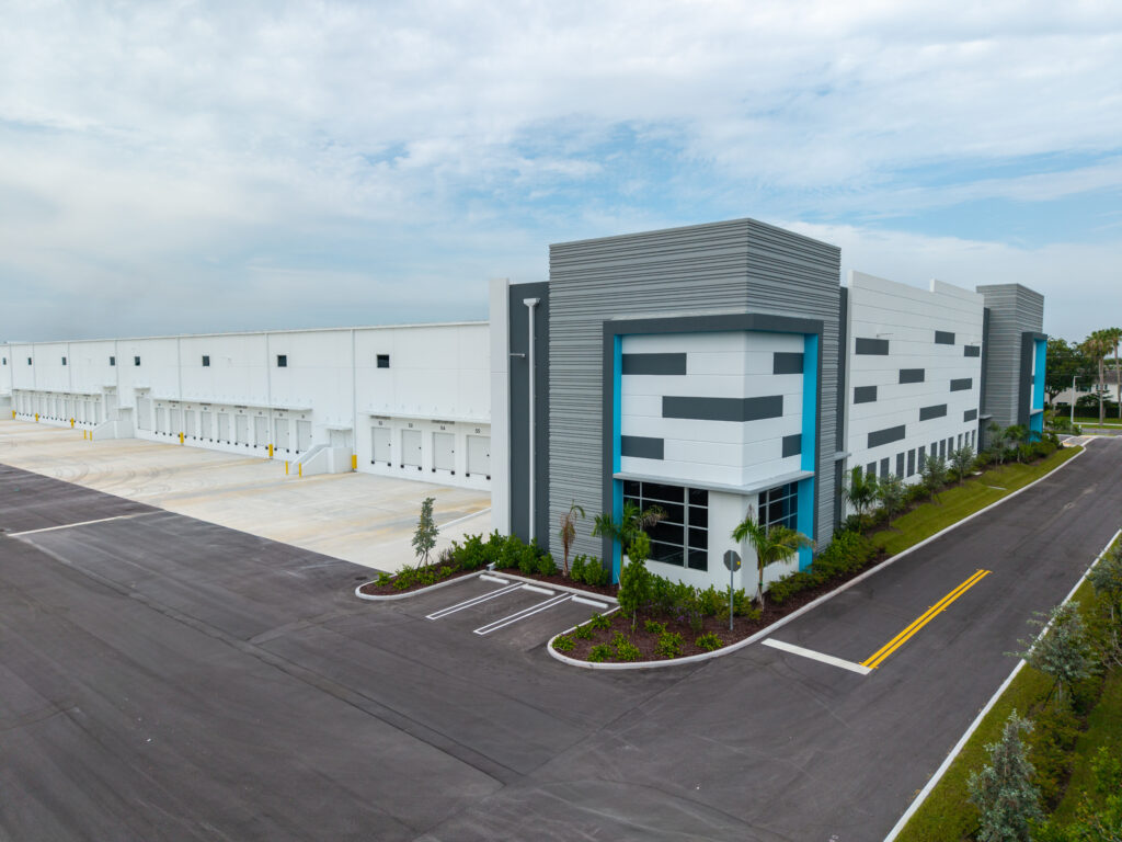 An aerial view of a large, modern industrial warehouse with multiple loading docks and a corner office space.