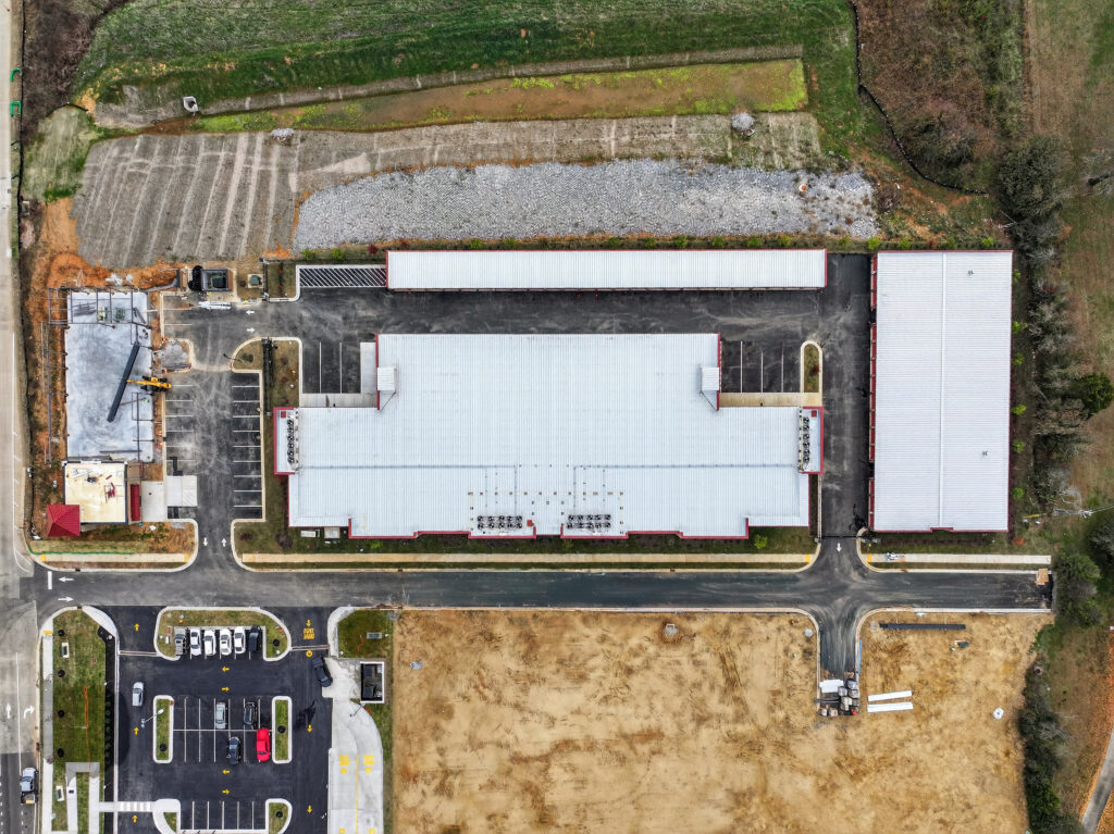 Aerial view of a self-storage facility with several buildings, a paved parking lot, and an adjacent construction site.