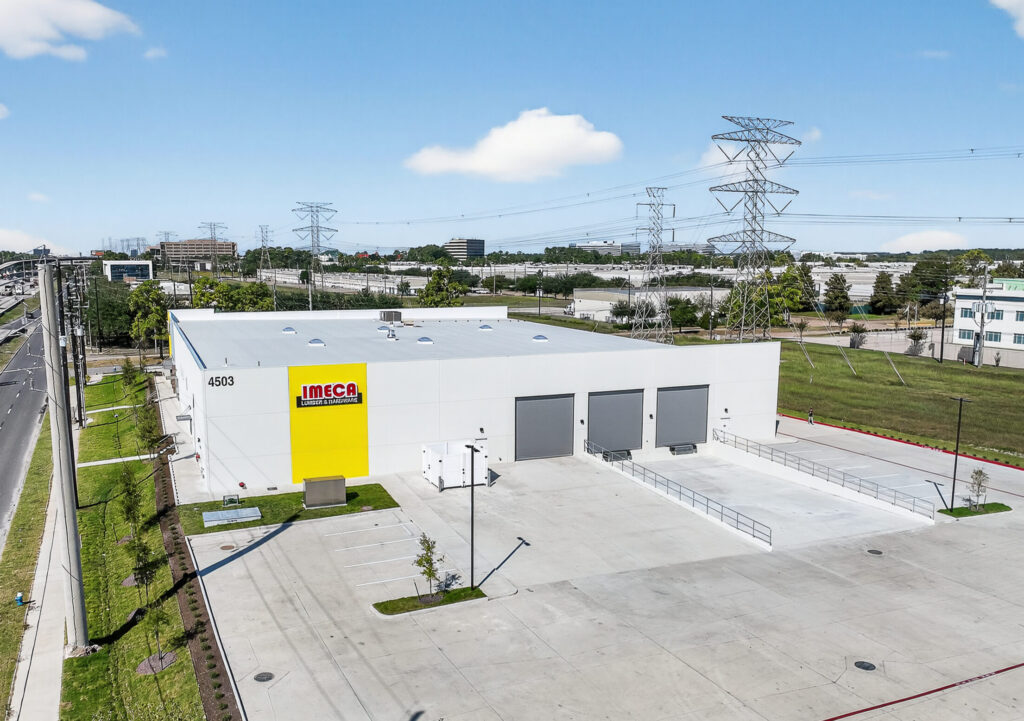 Aerial view of the Imeca Lumber & Hardware warehouse building with loading docks, parking area, and nearby power lines.