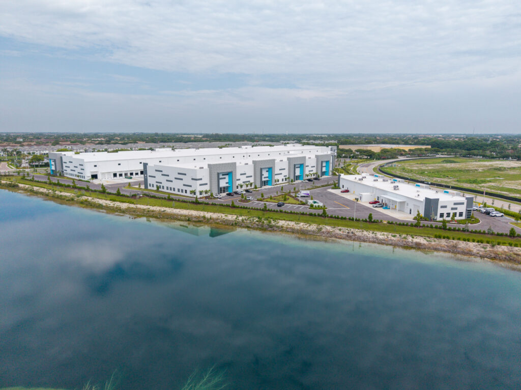 Aerial view of two modern industrial warehouse buildings situated along a lakefront.